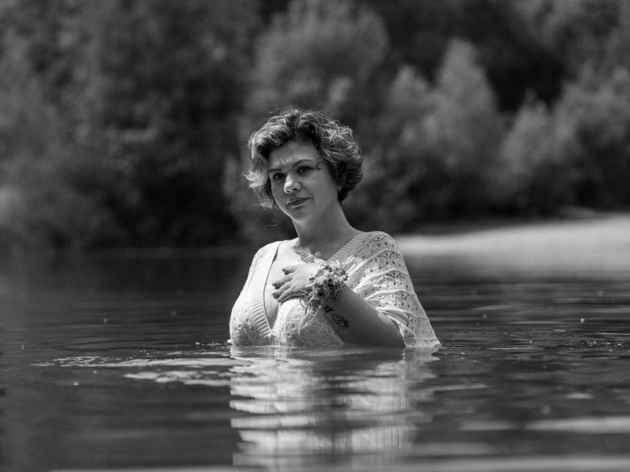 Frau mit Blumenkranz in einem Gewässer, umgeben von Bäumen im Hintergrund.Empowerment und Portraitfotografie in Schleswig Holstein