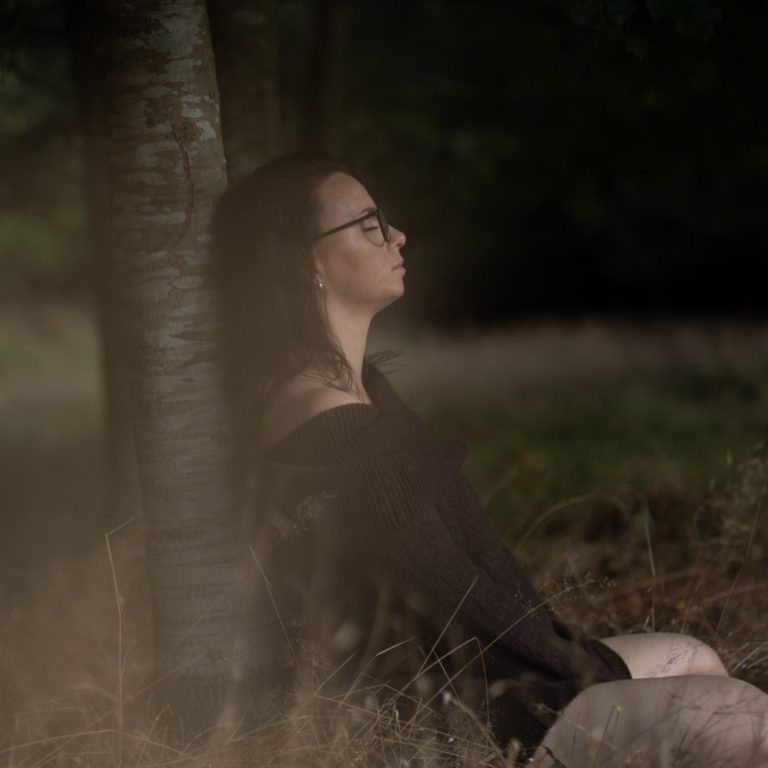 Verwurzelt: bei dir selbst zuhause sein | Body & Soul Stories Frau lehnt mit geschlossenen Augen an einem Baumstamm im Abendlicht, achtsames Fotoshooting Verwurzelt