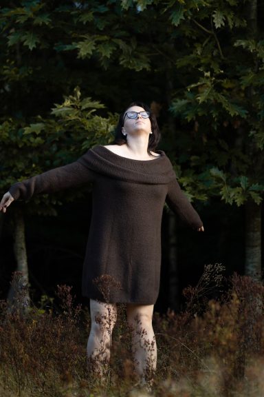 Frau steht mit ausgebreiteten Armen im Abendlicht im Grünen, Moment von Selbstannahme beim Empowerment Fotoshooting