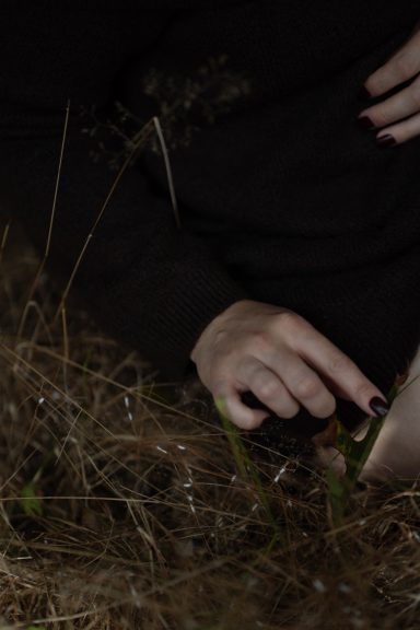 Hände einer Frau berühren Gras, Detailaufnahme im Dunkeln, Empowerment Fotoshooting in der Natur